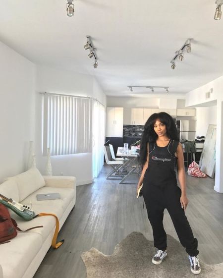 sza standing in her living room wearing full black champions outfit 